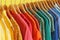 Bright clothes on hangers against yellow, closeup. Rainbow colors