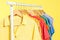 Bright clothes hanging on rack against yellow, closeup. Rainbow colors