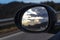 Bright cloudscape reflecting on an oval black mirror car while driving