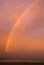 Bright colorful double rainbow during sunset with gloomy blurred red shimmering sky over the ocean