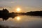 Bright and colorful sunset on the river. The sun hides behind the trees in the evening. Glare of the setting sun on the water