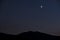 Bright crescent in dark sky over mountains