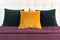 Bright decorative soft pillows in bed on the background of leather quilted headboard. Emerald and orange pillow, part of bed close