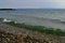 bright emerald green waves of lake baikal in the light of the sun in summer, blue mountains on horizon, stones in water, coast