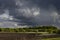 Bright epic thunderstorm landscape in early spring with dark blue fluffy clouds in sunlights above black field arable land.