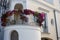 Bright flowers in pots on round balcony of white building. House facade decorated with flowerpots.