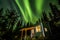 Bright green Aurora Borealis over small green and white tiny house in Alaska
