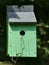 Bright Green Bird House with a Gray Roof. Grass or Straw coming out of the hole