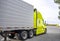 Bright green bonnet big rig semi truck transporting cargo in refrigerator semi trailer running out of truck stop parking lot