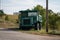 Bright green dump truck with funny eyes parked in a field under a cloudy sky