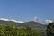 Bright green foliage against the background of wooded hills and the snow ridge of the Annapurna Mountains under a clear blue sky