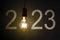 Bright light bulb with number 2023 on concrete wall