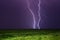 Bright lightnings in dark stormy sky above green field, climate change or weather forecast concept image