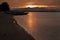 Bright majestic golden sunset on ocean with dark silhouette volcano, boat on shore, black coastline, orange saturated reflection.