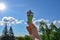 Bright multi-colored ice cream in hand against background of clear blue summer sky and green trees. Highly raised female hand