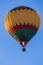 A bright multicolored hot air balloon with an expansive burner flame soars up against a background of blue sky.