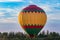 A bright multicolored hot air balloon at the moment of light touch with the ground on a forest lawn against a blue sky during suns