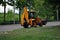 Bright orange excavator tractor on the road along park, spring in Kharkiv