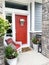 Bright orange front door and porch with a wicker chair. Colorful entrance