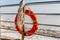 Bright orange lifebuoy to help a drowning man, tied with ropes to a metal railing, against the backdrop of a frozen sea