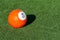 Bright orange number 5 soccer billiards or pool ball on green grass with a shadow and copy space. Concept of sports, recreation