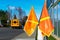 Bright orange pedestrian crossing flags at a crosswalk near school. Blurred school bus in background