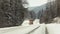 Bright orange plough truck cleaning snow on forest road in winter, view from car driving other way, trees around