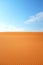 Bright orange rippled desert sand and clear blue sky with straight horizon