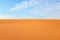 Bright orange rippled desert sand and clear blue sky with straight horizon