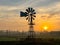 Bright orange sunrise at fields with light fog and an American style windmill