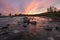 Bright orange sunset over wild river with big rocks and orange reflection