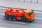 A bright orange truck with a tank for combustible fuel and other flammable liquids is driving along the highway