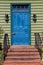 Bright painted blue door on a green house with brick steps