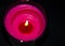 Bright pink candle in a glass jar on a black background. The candle is burning. Extinguished candle. Smoke from the candle. Hearth