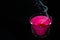 Bright pink candle in a glass jar on a black background. The candle is burning. Extinguished candle. Smoke from the candle. Hearth