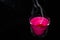 Bright pink candle in a glass jar on a black background. The candle is burning. Extinguished candle. Smoke from the candle. Hearth