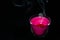 Bright pink candle in a glass jar on a black background. The candle is burning. Extinguished candle. Smoke from the candle. Hearth