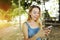 Bright portrait with sunshine of young blonde girl chatting by smartphone and riding swing in Bali, sand in background.