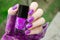 Bright purple Nail art manicure. Holiday style nails with neon glitter. Woman holds Bottle of Nail Polish