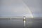 Bright rainbow high in sky over lighthouse in sea during dark storm