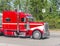 Bright red big rig classic American bonnet semi truck driving on intersection with traffic light
