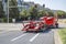 Bright red big rig classic car hauler semi truck with empty hydraulic semi trailer turning on the crossroad street section