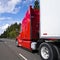 Bright red big rig long haul semi truck with high cabin transporting cargo in semi trailer driving on multiline road