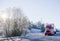 Bright red big rig semi truck with refrigerator semi trailer transporting cargo on straight winter highway frosty hill trees