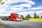 Bright red big rig semi truck tractor with loaded flat bed semi trailer standing on the road in industrial area