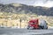 Bright red big rig semi truck tractor towing another semi truck tractor with the rear wheels raised and fixed on the fifth wheel