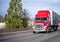 Bright red big rig semi truck transporting cargo in semi trailer running on the turning highway road