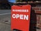 Bright red `Businesses Open` sign on a street corner in a busy downtown area