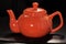 Bright red ceramic teapot or brewing teapot on a black background. Small kettle, afternoon tea-drink hot tea