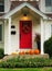 Bright red front door on a white house with a variety of pumpkins lined up on the porch.